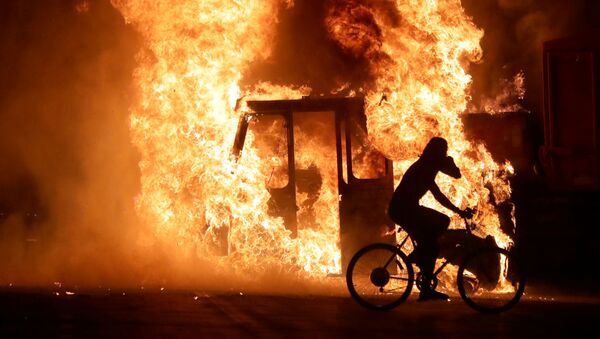 Homem de bicicleta passa em frente a caminhão em chamas na frente ao Tribunal do condado de Kenosha, no estado de Wisconsin, nos Estados Unidos, após protesto pelos tiros disparados pela polícia contra o homem negro Jacob Blake.  - Sputnik Brasil