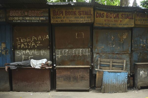 Homem dorme em frente a livrarias fechadas durante o isolamento diurno imposto em meio ao aumento de casos de COVID-19 em Calcutá - Sputnik Brasil