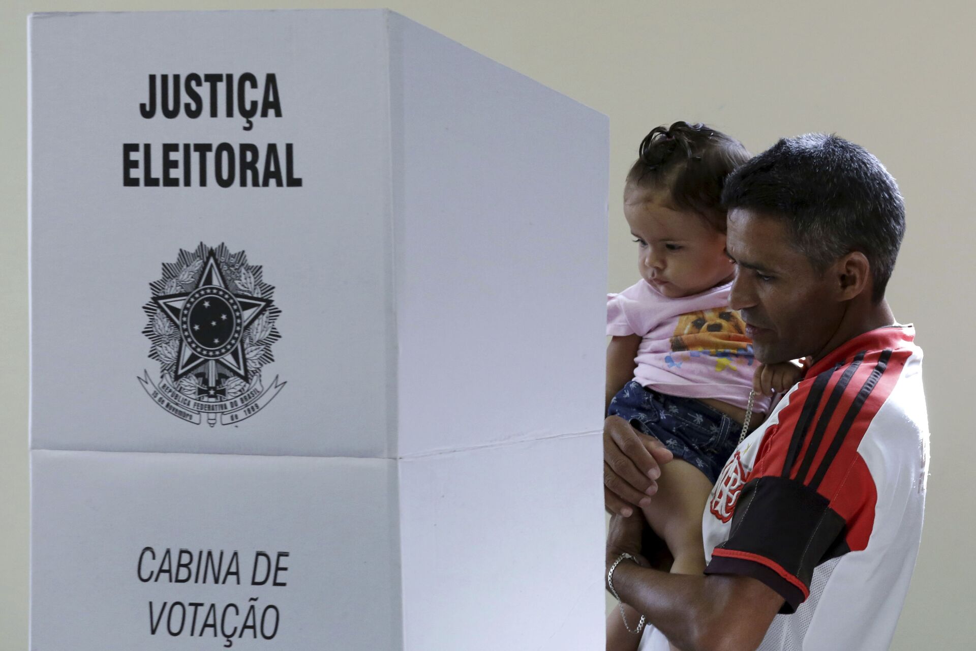 Em Brasília, um homem com um bebê nos braços deposita seu voto em uma urna eletrônica durante as eleições gerais no Brasil, em 28 de outubro de 2018. - Sputnik Brasil, 1920, 15.03.2022