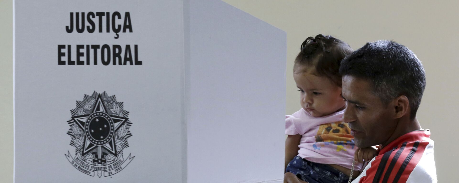 Em Brasília, um homem com um bebê nos braços deposita seu voto em uma urna eletrônica durante as eleições gerais no Brasil, em 28 de outubro de 2018. - Sputnik Brasil, 1920, 05.05.2022