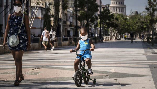 Em Havana, Cuba, uma mulher acompanha uma criança que anda de bicicleta enquanto ambos usam máscaras de proteção devido à pandemia da COVID-19, em 3 de julho de 2020. - Sputnik Brasil
