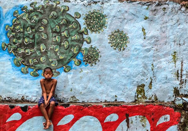 Garoto sentado diante de mural com desenho do vírus responsável pela COVID-19 em Bogor, na Indonésia - Sputnik Brasil