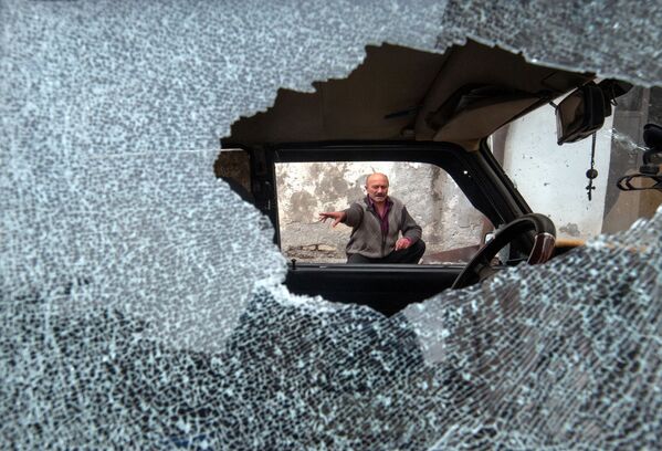 Homem diante de carro com vidros quebrados em resultado dos ataques à cidade de Stepanakert, em Nagorno-Karabakh - Sputnik Brasil
