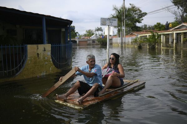 Homem utiliza porta como jangada improvisada enquanto transporta uma mulher pelas ruas inundadas no bairro Mata Redonda, em Maracay, Venezuela
 - Sputnik Brasil
