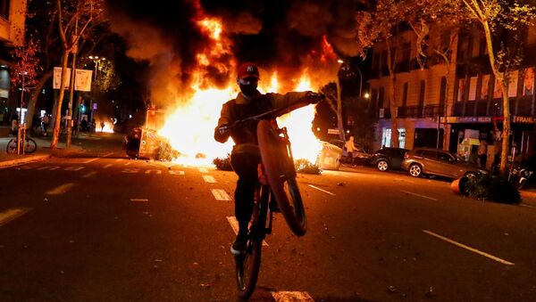 Em Barcelona, na Espanha, um homem empina uma bicicleta em frente a uma barricada em chamas durante protesto contra a quarentena da COVID-19, em 30 de outubro de 2020 - Sputnik Brasil