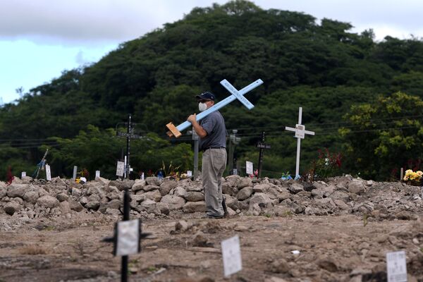 Homem com cruz olha para sepulturas no cemitério COVID-19 no Dia dos Mortos em Honduras - Sputnik Brasil