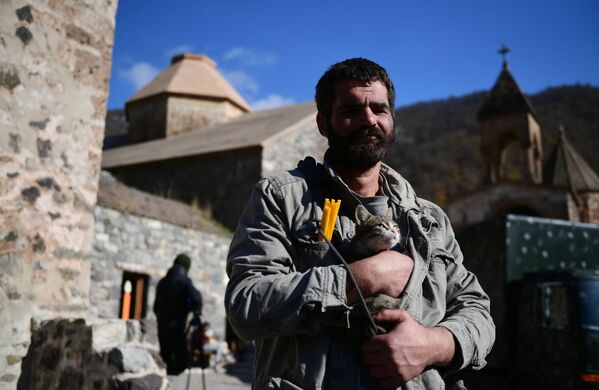 Homem segura um gato perto de um templo no mosteiro de Dadivank em Nagorno-Karabakh
 - Sputnik Brasil