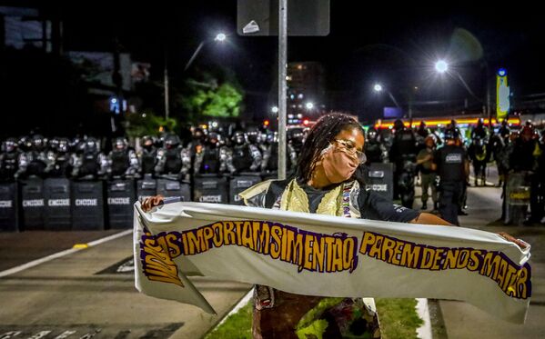 Mulher negra segura uma faixa em frente a tropa de choque durante o protesto contra a morte de João Alberto Silveira Freitas, após o mesmo ter sido morto por seguranças brancos no supermercado Carrefour em Porto Alegre, 23 de novembro, 2020. - Sputnik Brasil
