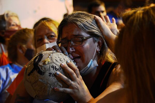 Mulher chora com uma bola de futebol, após a morte Diego Maradona na Argentina. - Sputnik Brasil