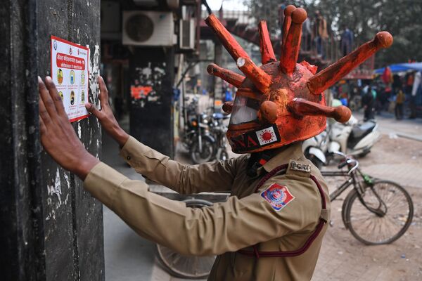 Voluntário com máscara temática do coronavírus exibe cartaz informativo em mercado de Nova Deli, na Índia - Sputnik Brasil
