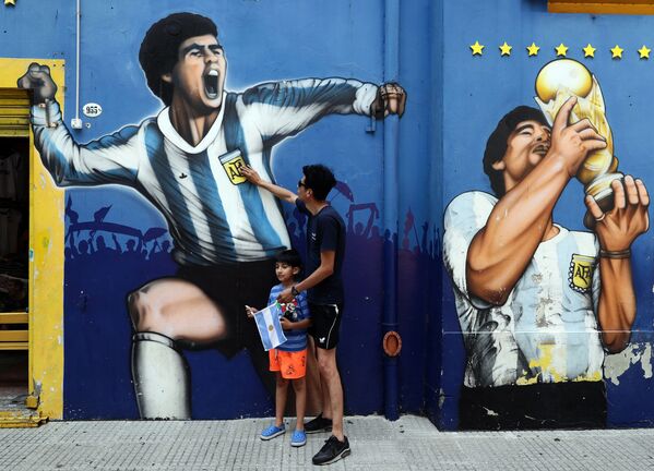 Homem e criança diante de grafites do ídolo do futebol Diego Maradona em Bueno Aires - Sputnik Brasil