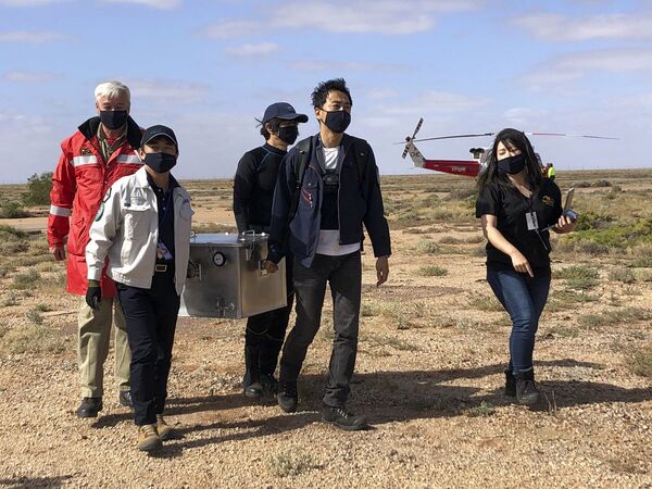 Em Woomera, na Austrália, grupo de pessoas leva caixa contendo amostras coletadas pela sonda espacial japonesa Hayabusa2 - Sputnik Brasil