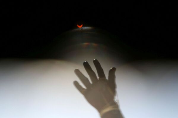 Eclipse solar é visto através de óculos de sol com filtros especiais em frente a uma estátua, em Santiago, Chile, 14 de dezembro de 2020 - Sputnik Brasil