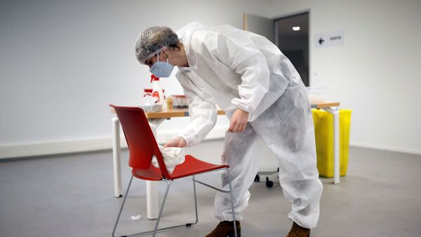 Um médico de macacão de proteção e máscara desinfecta uma cadeira no centro de testes de coronavírus em Rezé, França, 15 de dezembro de 2020 - Sputnik Brasil
