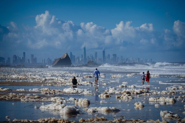 Turistas caminham na espuma marinha depois das condições ciclônicas na praia Currumbin Beach, Austrália, que provocaram chuva e vento fortes nas regiões de Nova Gales do Sul e Sudeste de Queensland, 15 de dezembro de 2020 - Sputnik Brasil