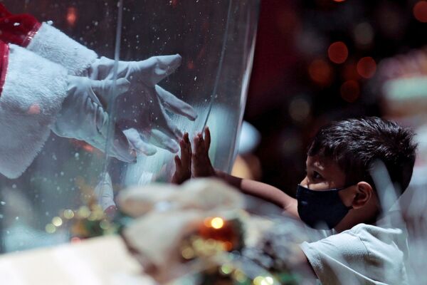 Abilio da Cruz Pinto, 77, vestido de Papai Noel dentro de bolha de plástico, cumprimenta uma criança em centro comercial durante surto da COVID-19 em Brasília, Brasil, 15 de dezembro de 2020 - Sputnik Brasil