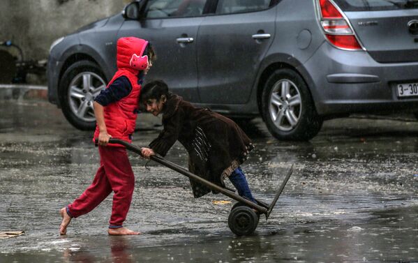 Menina palestina empurra outra montando um carro de mão durante um dia chuvoso no sul da Faixa de Gaza, 16 de dezembro de 2020 - Sputnik Brasil
