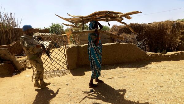 Um pacificador da Operação Híbrida das Nações Unidas em Darfur (UNAMID) acompanha uma mulher sudanesa carregando lenha na cabeça enquanto ela caminha pelo campo de Kalma para pessoas deslocadas internamente em Darfur, Sudão - Sputnik Brasil