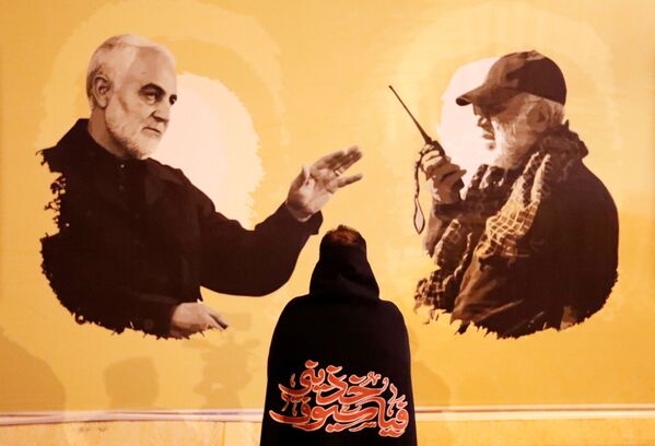 Pessoa observa banner com as fotos do major-general iraniano Qassem Soleimani e do líder da milícia xiita iraquiana Abu Mahdi al-Muhandis no aniversário de um ano da morte de ambos em operação dos EUA no Iraque - Sputnik Brasil