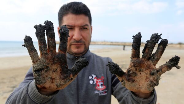 Homem mostra alcatrão nas mãos na sequência de um derramamento que alagou grande parte da costa do Mediterrâneo - Sputnik Brasil