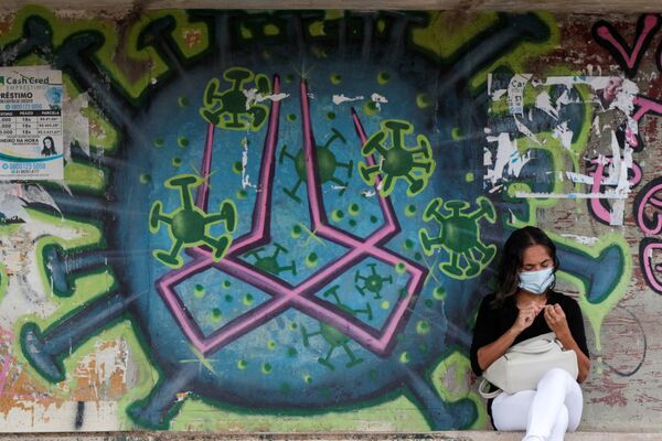 Mulher sentada em frente a um grafite retratando coronavírus, Brasília, 11 de março de 2021 - Sputnik Brasil
