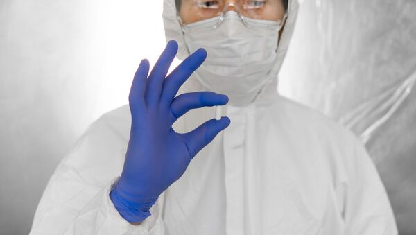 Médico em traje de proteção branco, máscara médica e luvas de borracha está segurando uma pílula branca como medicamento contra a ameaça de pandemia de coronavírus. - Sputnik Brasil
