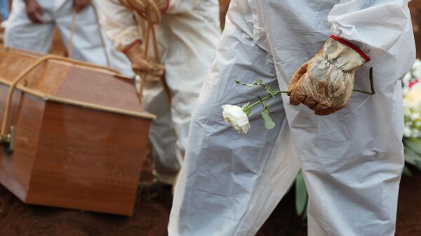 Coveiro com traje de proteção segura flor durante enterro de pessoa falecida por COVID-19 no Cemitério da Vila Formosa, em São Paulo, no Brasil, no dia 23 de março de 2021 - Sputnik Brasil