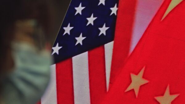 Mulher usando máscara sentada perto de uma tela que mostra bandeiras da China e dos EUA - Sputnik Brasil