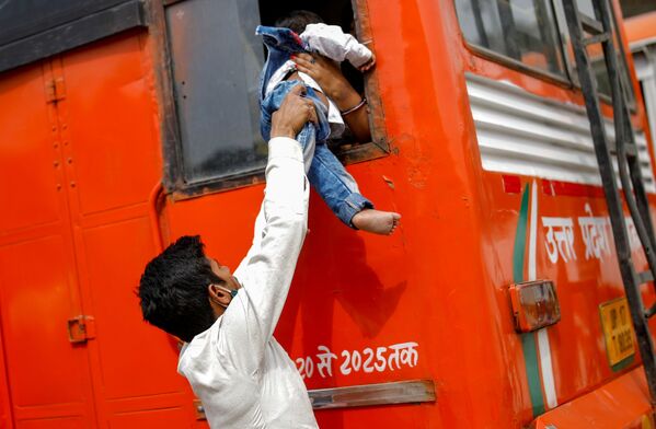 Trabalhador migrante passa seu filho através de janela de ônibus no regresso a seu povoado, após o governo de Deli ter anunciado o confinamento de seis dias para parar a propagação da COVID-19, em Gaziabade, arredores de Nova Deli, Índia, 20 de abril de 2021 - Sputnik Brasil