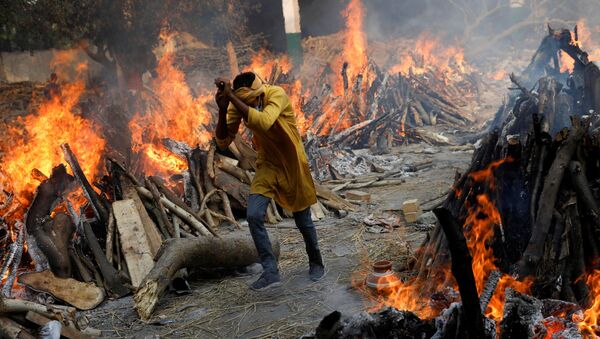 Em Nova Deli, na Índia, um homem corre em meio a piras funerárias em meio a uma cremação em massa de corpos de pacientes infectados com a COVID-19, em 26 de abril de 2021 - Sputnik Brasil