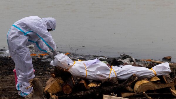 Homem usando traje de proteção toca no corpo de seu parente que morreu de COVID-19 antes de sua cremação nas margens do rio Ganges em Garhmukteshwar, no estado de Uttar Pradesh, Índia, 6 de maio de 2021 - Sputnik Brasil