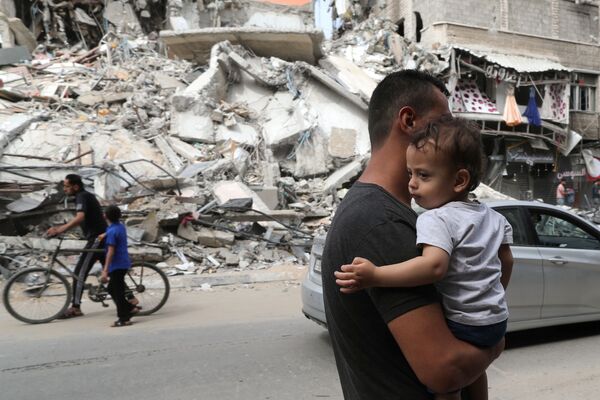Palestino segura criança enquanto passa perto das ruínas de um prédio destruído pelo ataque aéreo israelense no conflito recente entre Israel e o Hamas, 21 de maio de 2021
 - Sputnik Brasil