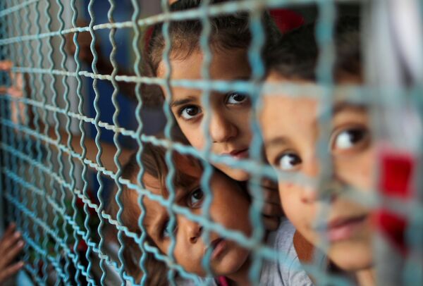 Crianças palestinas, que abandonaram suas casas por causa dos ataques aéreos e de artilharia de Israel, olham através da cerca da escola sob gerência da ONU, Faixa de Gaza, 18 de maio de 2021 - Sputnik Brasil
