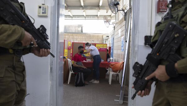Soldados israelenses montam guarda enquanto um palestino que trabalha em Israel recebe uma vacina Moderna COVID-19 no cruzamento Tarkumiya entre a Cisjordânia e Israel, segunda-feira, 8 de março de 2021 - Sputnik Brasil