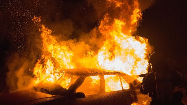 Carro incendiado com fogo sendo apagado por bombeiro - Sputnik Brasil