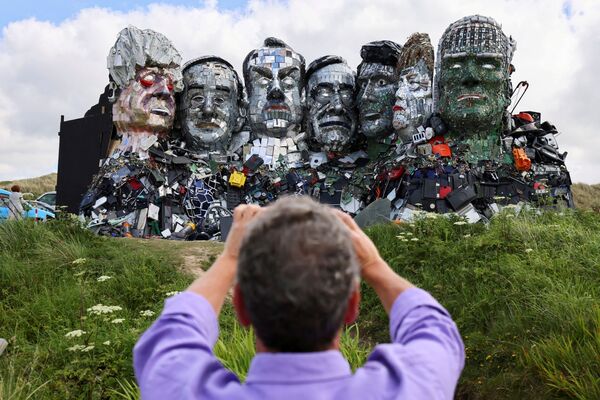 Homem faz fotos da obra de Joe Rush e Alex Wreckage Monte Recicla Mais, feita a partir de resíduos eletrônicos, retratando os líderes do G7, em Hayle Towans, na Cornualha, Grã-Bretanha, 8 de Junho de 2021 - Sputnik Brasil