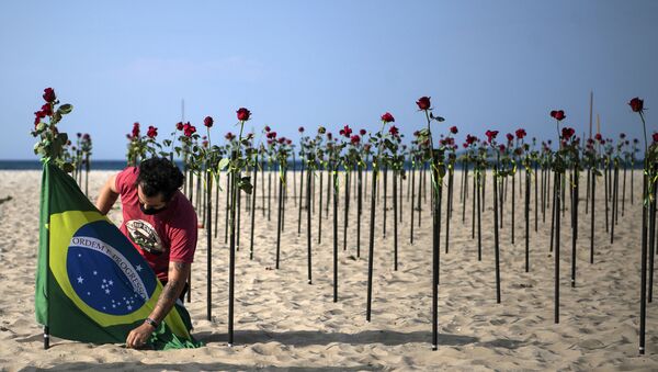 Manifestante coloca bandeira brasileira ao lado das rosas depostas pela ONG Rio de Paz na praia de Copacabana em homenagem a mais de meio milhão de mortes pela COVID-19 no país, 20 de junho de 2021 - Sputnik Brasil