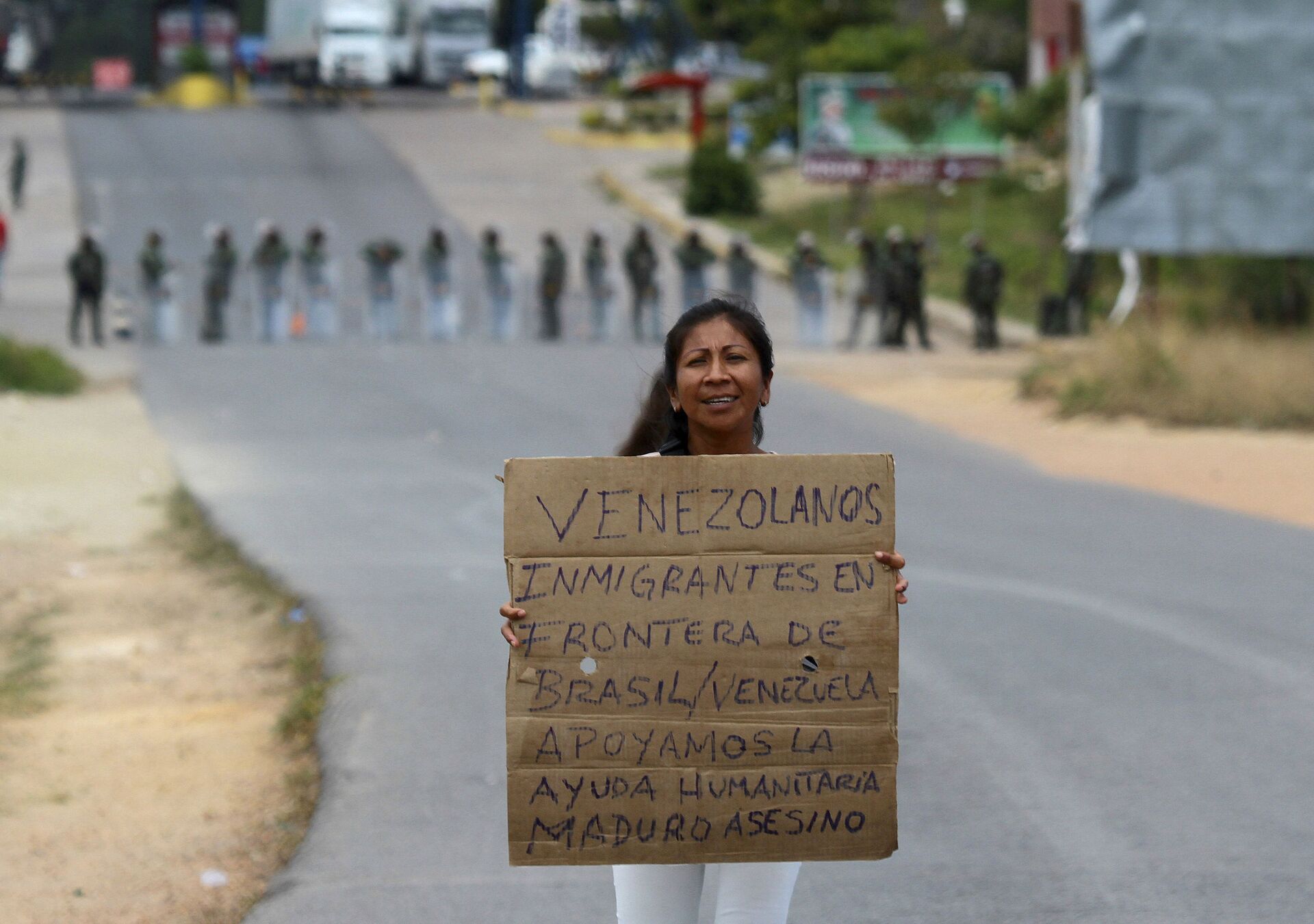 Venezuelana segura uma placa que diz em espanhol Migrantes venezuelanos na fronteira Brasil-Venezuela, apoiamos a ajuda humanitária. Maduro assassino enquanto aguarda a abertura da fronteira em Pacaraima, em Roraima, Brasil (foto de arquivo) - Sputnik Brasil, 1920, 28.12.2021