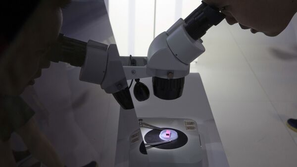 Visitante da 21ª China Beijing International High-Tech Expo olha para chip de computador pelo microscópio exibido pela fabricante estatal Tsinghua Unigroup, que emergiu como campeã nacional das ambições de semicondutores de Pequim, em 17 de maio de 2018 - Sputnik Brasil