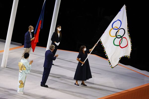 A prefeita de Paris, Anne Hidalgo, agita a bandeira olímpica durante a cerimônia de encerramento dos Jogos Olímpicos de Tóquio enquanto o presidente do Comitê Olímpico Internacional, Thomas Bach, e o governadora de Tóquio, Yuriko Koike, aplaudem - Sputnik Brasil