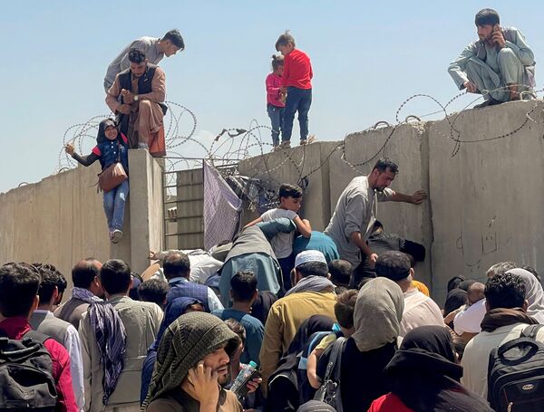 Homem ajuda menina a entrar no Aeroporto Internacional de Hamid Karzai através do muro, enquanto multidões tentam fugir do país, Cabul, Afeganistão, 16 de agosto de 2021 - Sputnik Brasil