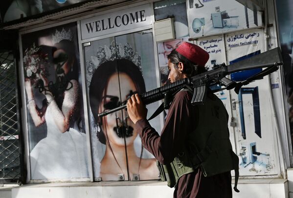 Militante do Talibã (organização terrorista proibida na Rússia e em vários outros países) passa por um salão de beleza com imagens de mulheres cobertas com tinta em Cabul, Afeganistão, 18 de agosto de 2021 - Sputnik Brasil