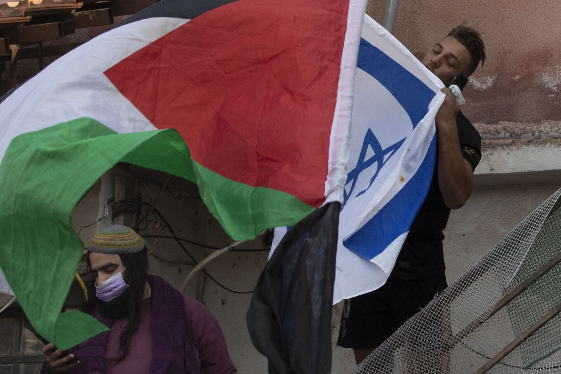 Um homem beija a bandeira israelense enquanto manifestantes agitam a bandeira palestina no portão da frente de uma casa palestina ocupada por judeus israelenses, 26 de maio de 2021 - Sputnik Brasil, 1920, 12.07.2022