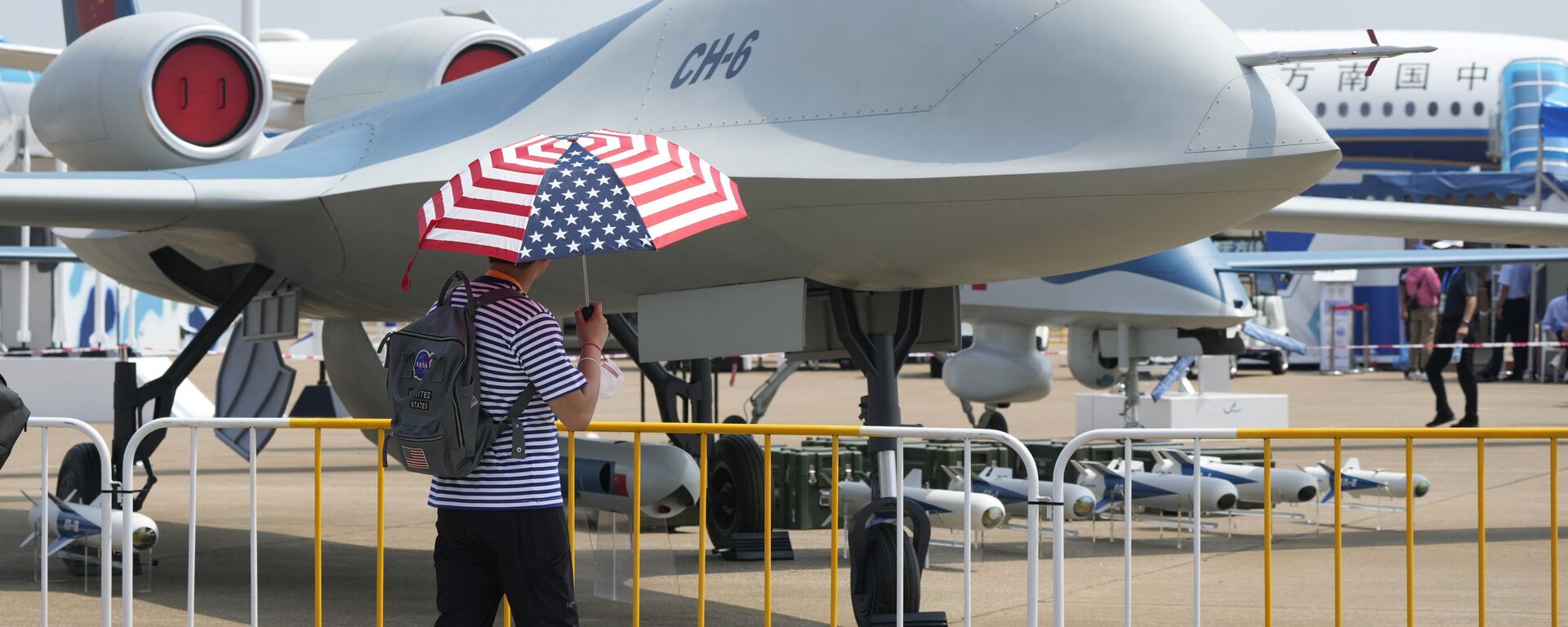 Homem com guarda-chuva com o desenho da bandeira dos EUA passa por um drone CH-6, em 28 de setembro de 2021 - Sputnik Brasil, 1920, 02.09.2022