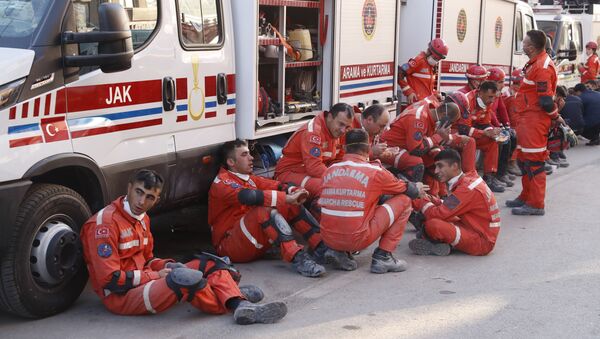 Membros dos serviços de resgate fazem pausa na busca de sobreviventes nos escombros de um prédio desabado em Izmir na Turquia - Sputnik Brasil