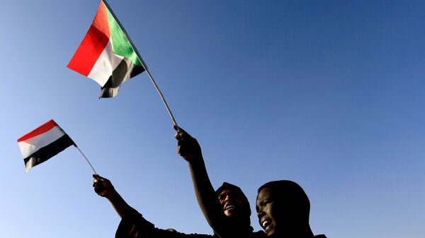 Sudaneses agitam sua bandeira nacional enquanto se reúnem na praça da liberdade durante o primeiro aniversário do início do levante que derrubou o governante de longa data Omar al-Bashir, em Cartum, Sudão, 19 de dezembro de 201 - Sputnik Brasil