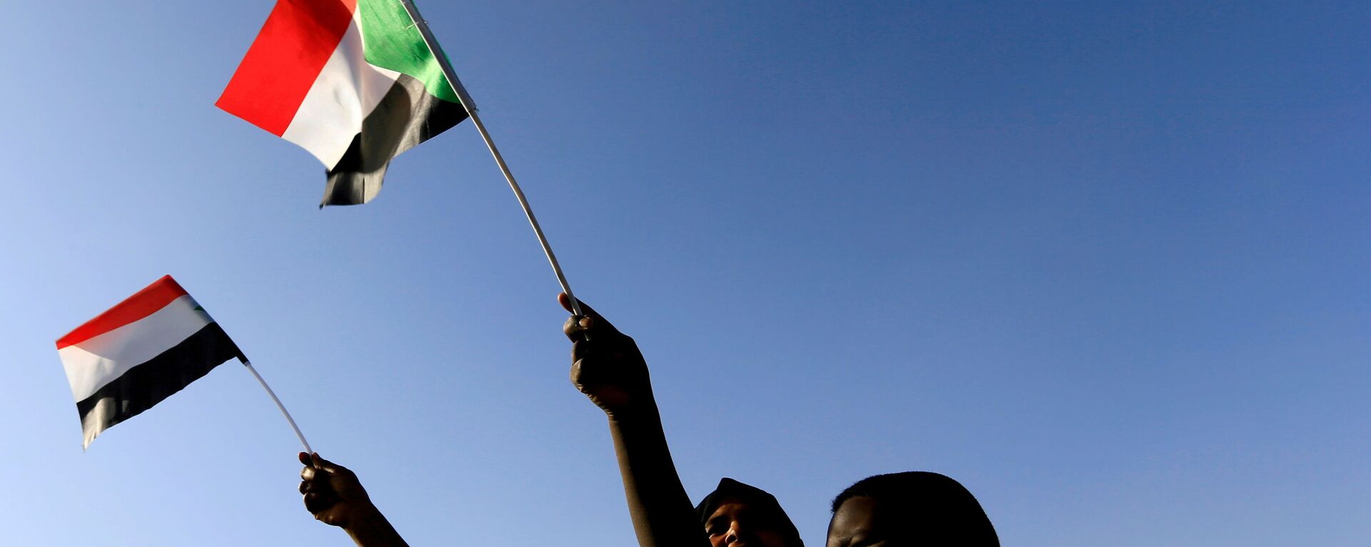 Sudaneses agitam sua bandeira nacional enquanto se reúnem na praça da liberdade durante o primeiro aniversário do início do levante que derrubou o governante de longa data Omar al-Bashir, em Cartum, Sudão, 19 de dezembro de 201 - Sputnik Brasil, 1920, 30.10.2021
