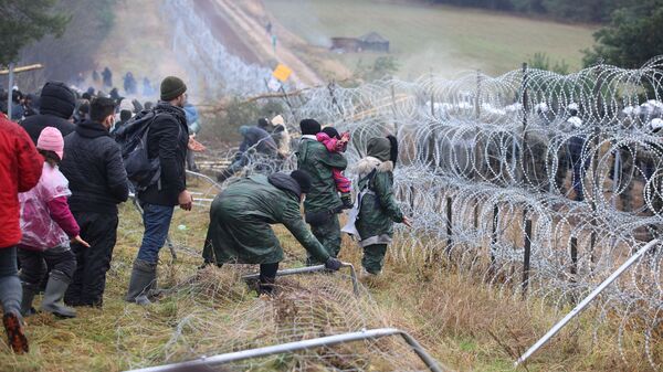 Migrantes se reúnem junto de cerca de arame farpado, com guardas fronteiriços poloneses do outro lado, para tentar cruzar a fronteira com a Polônia na região de Grodno, Belarus, 8 de novembro de 2021 - Sputnik Brasil