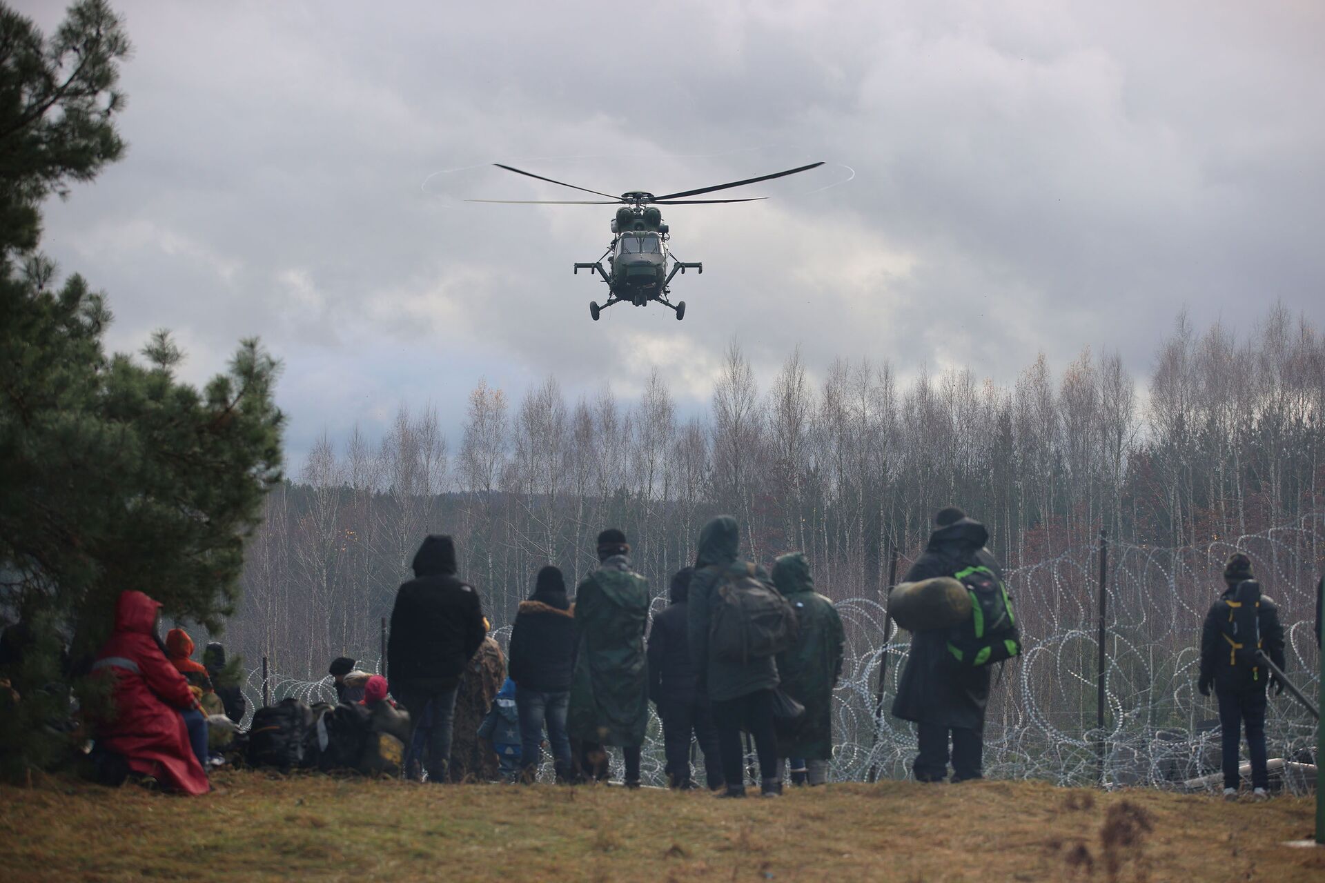 Migrantes se reúnem junto de cerca de arame farpado, com helicóptero sobrevoando a área, para tentar cruzar a fronteira com a Polônia na região de Grodno, Belarus, 8 de novembro de 2021 - Sputnik Brasil, 1920, 09.11.2021