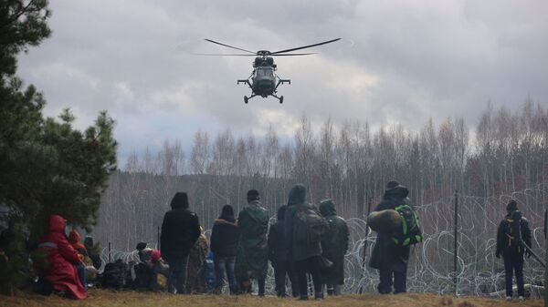 Migrantes se reúnem junto de cerca de arame farpado, com helicóptero sobrevoando a área, para tentar cruzar a fronteira com a Polônia na região de Grodno, Belarus, 8 de novembro de 2021 - Sputnik Brasil